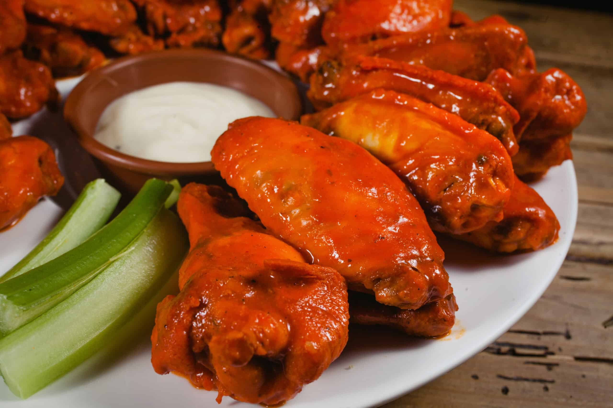 A plate of saucy buffalo chicken wings with a side of celery sticks and a small dish of creamy ranch dressing sits on a rustic wooden table, perfect for enjoying during an exciting World Cup match.