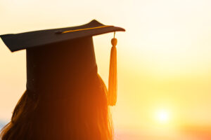 A person wearing a graduation cap with a tassel stands facing a golden sunset. The silhouette creates a warm, inspiring scene, symbolizing new beginnings and achievements.