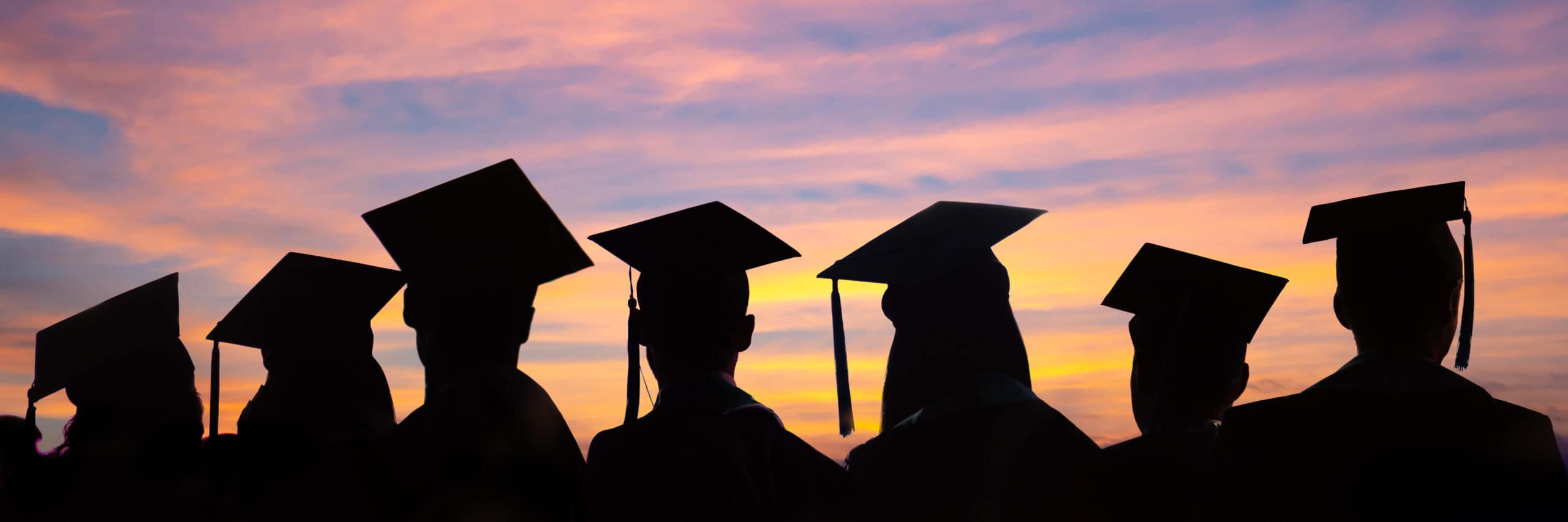 Silhouettes of graduates in caps and gowns stand together against a colorful sunset sky, celebrating their achievement as Deloitte Foundation Arizona Scholars.