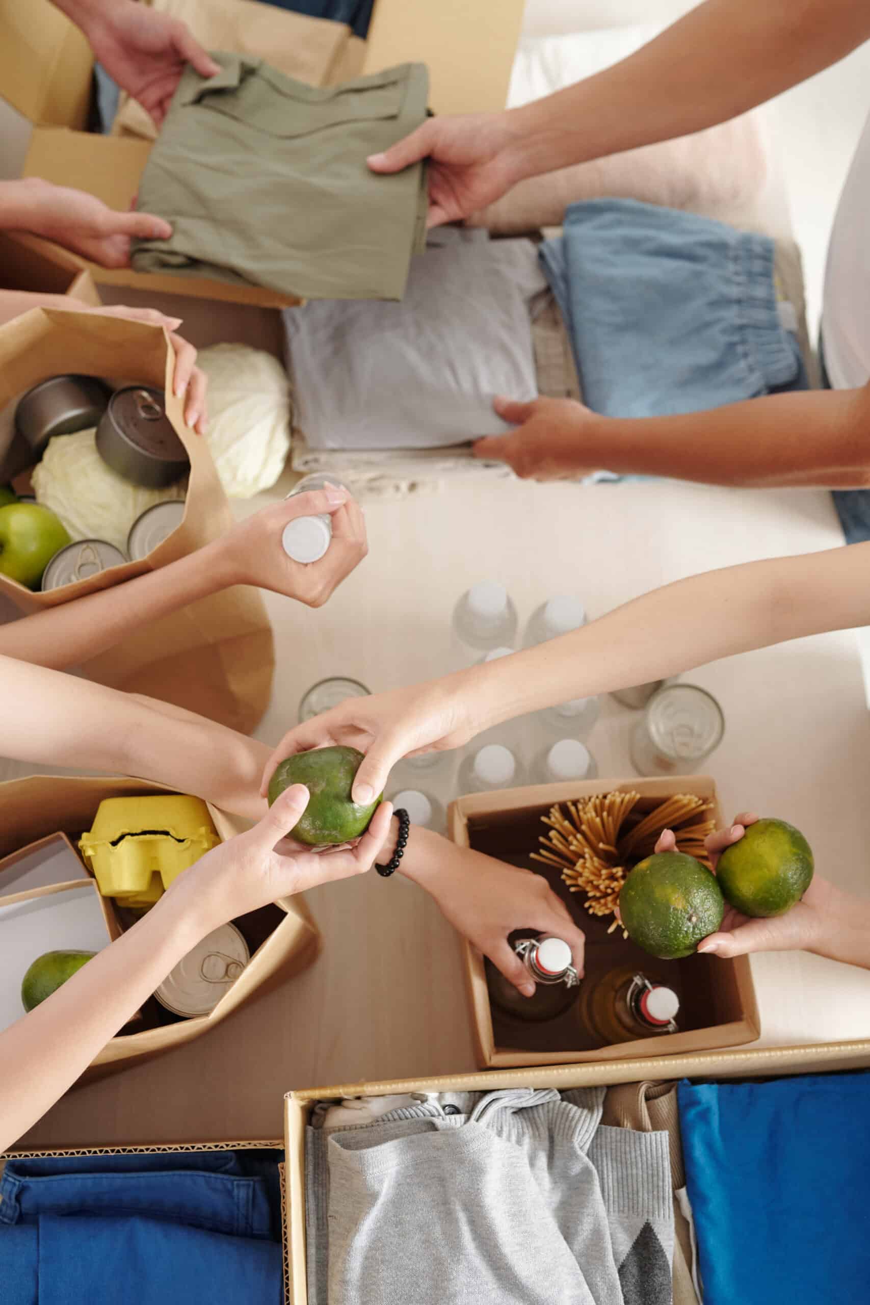 As seen from above, several people—recipients of the Arizona Community Service Awards—pack boxes with clothing, bottled drinks, canned food, apples, and other supplies, reaching in and passing items to each other.