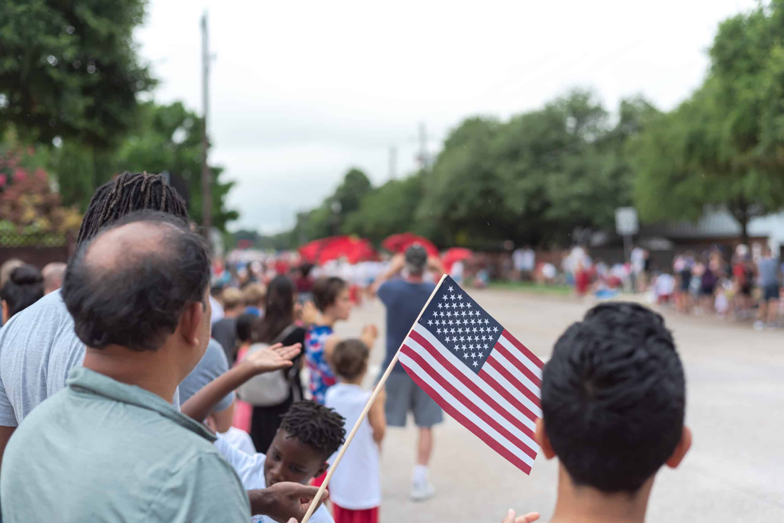 People watch a parade during the Summer of Civics, and one person proudly holds up a small American flag.