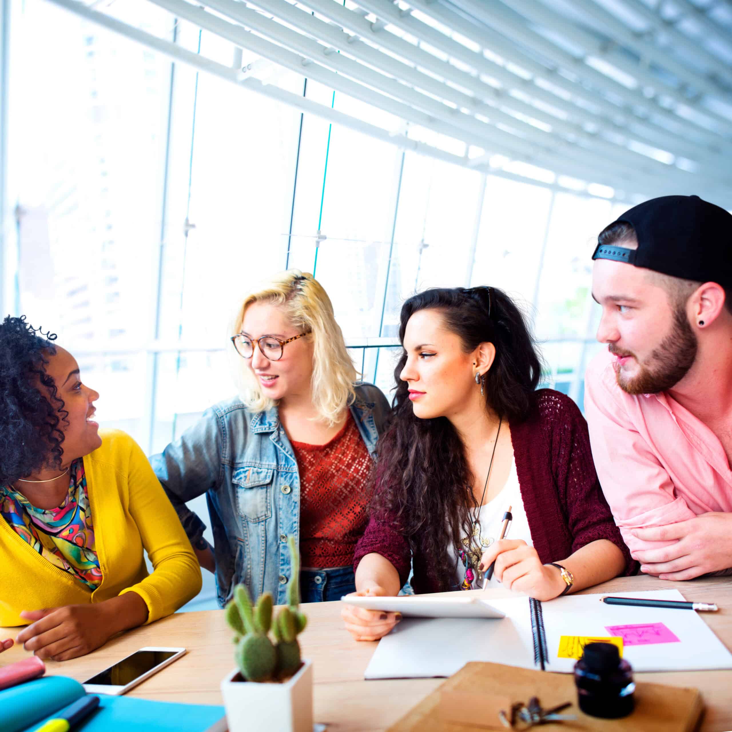 Four people sit at a table in a bright office, talking and reviewing a notebook that includes information on the Seal of Civic Literacy.
