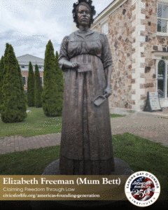 A bronze statue of Elizabeth Freeman (Mum Bett), known as The Citizen, stands outdoors on a brick walkway, with tall green shrubs and a stone building with large windows in the background.