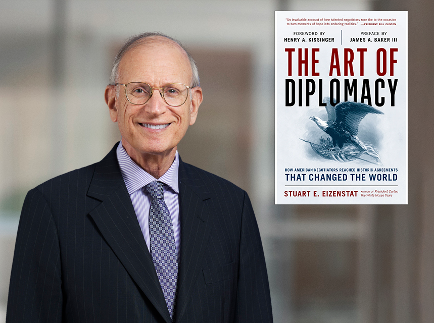 An older man in a suit and tie smiles at the camera. To his right is a book cover titled "The Art of Diplomacy" by Stuart E. Eizenstat, featuring an eagle and a globe illustration. The background is blurred.