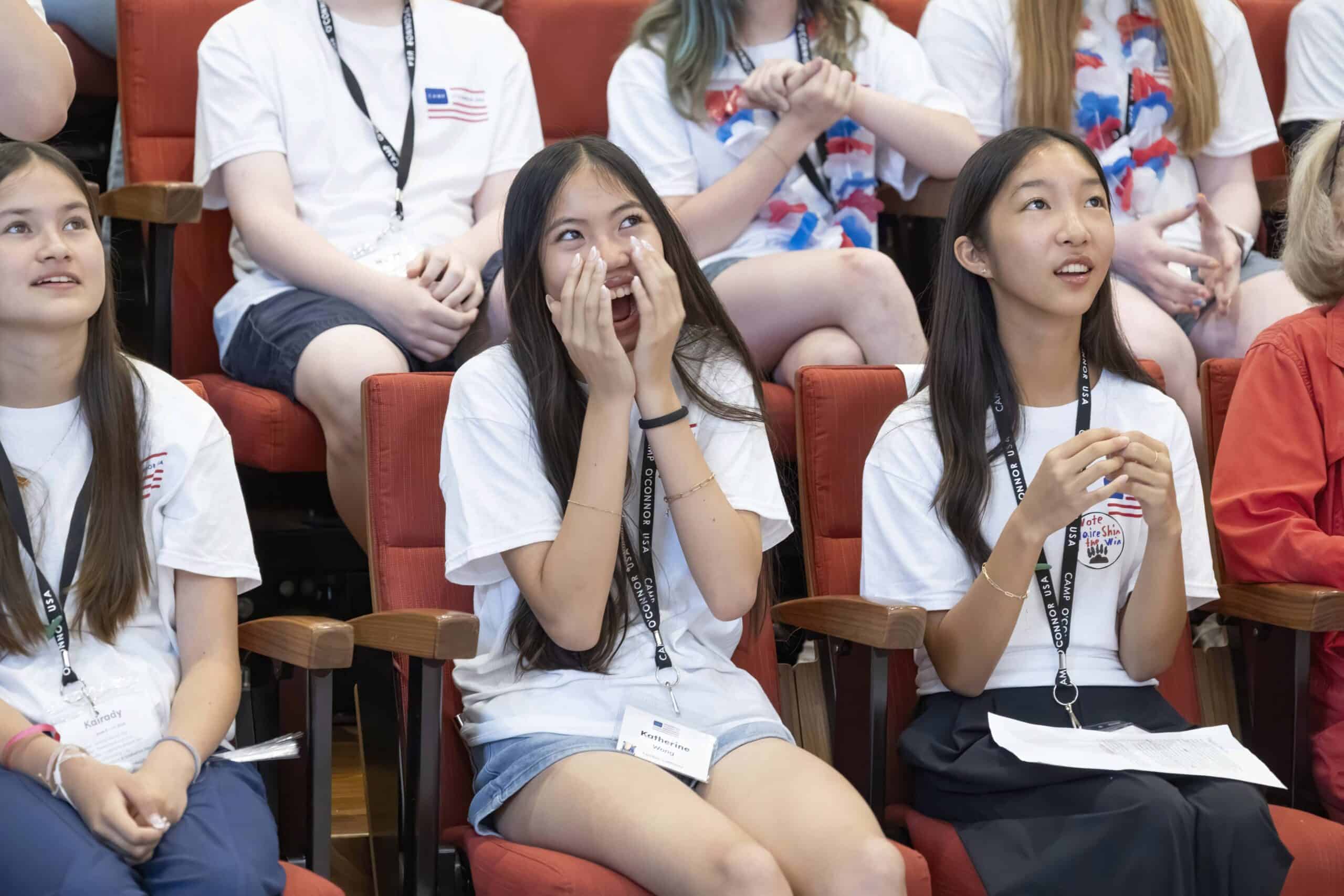 A group of students wearing white shirts sit in red chairs. The girl in the center is smiling with her hands on her face, while the others around her, perhaps future leaders from The Citizen, appear engaged and attentive.