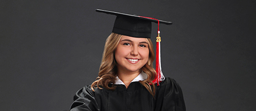 A graduate wearing a black cap and gown smiles against a dark background. The cap features a red and white tassel with the number "20" attached.