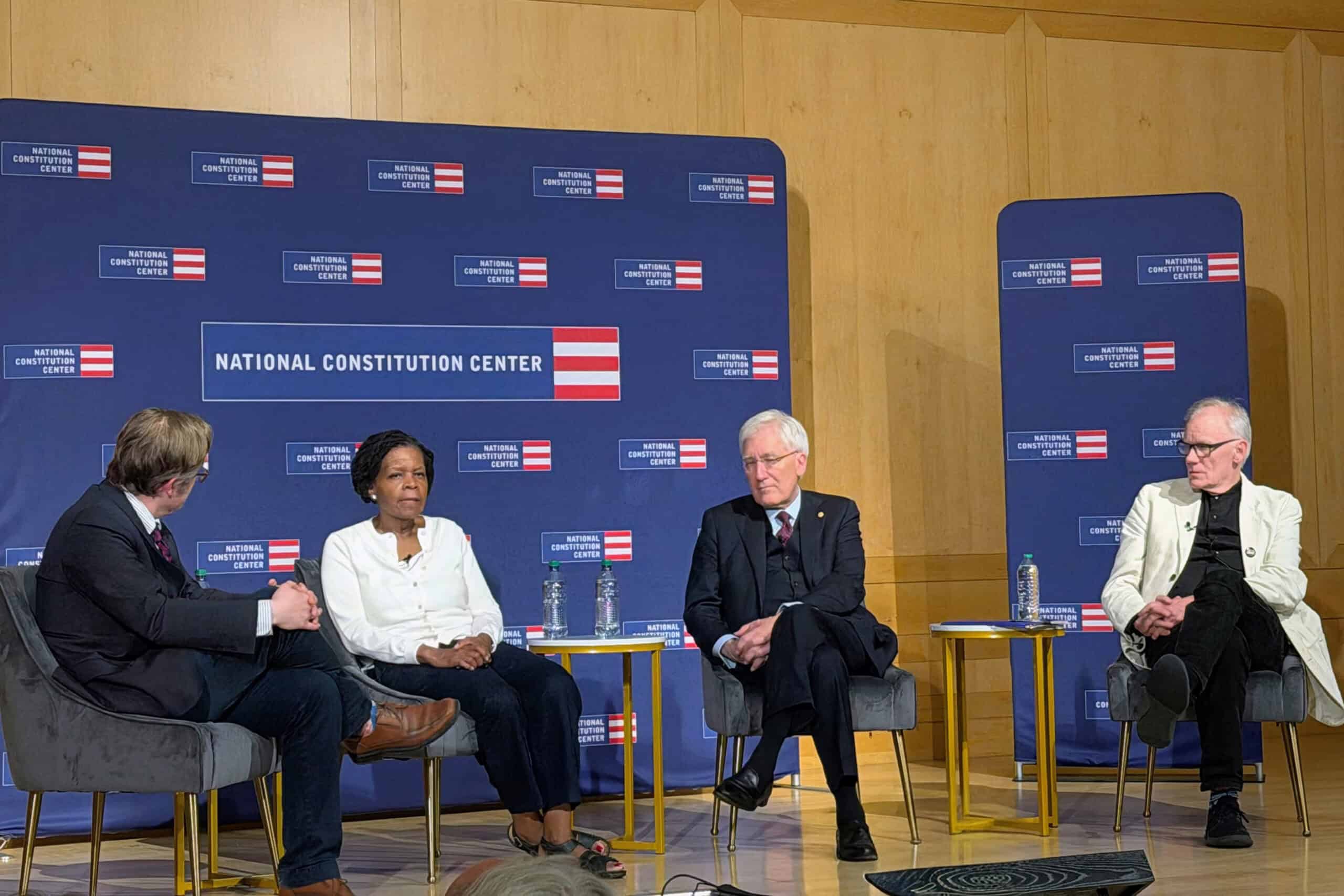 Four people sit on stage in discussion at the National Constitution Center, with The Citizen's logo and backdrop behind them. Three men and one woman are seated in chairs, facing each other, engaged in conversation.