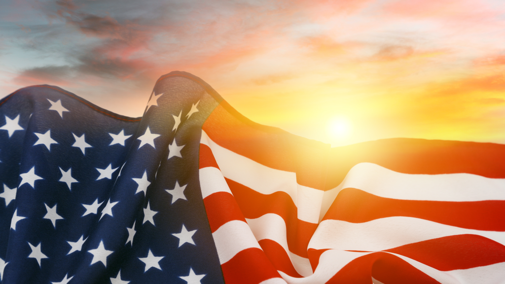 Close-up of the American flag with stars and stripes visible, set against a bright sunrise sky—an inspiring scene reflecting the spirit of the Summer of civics.
