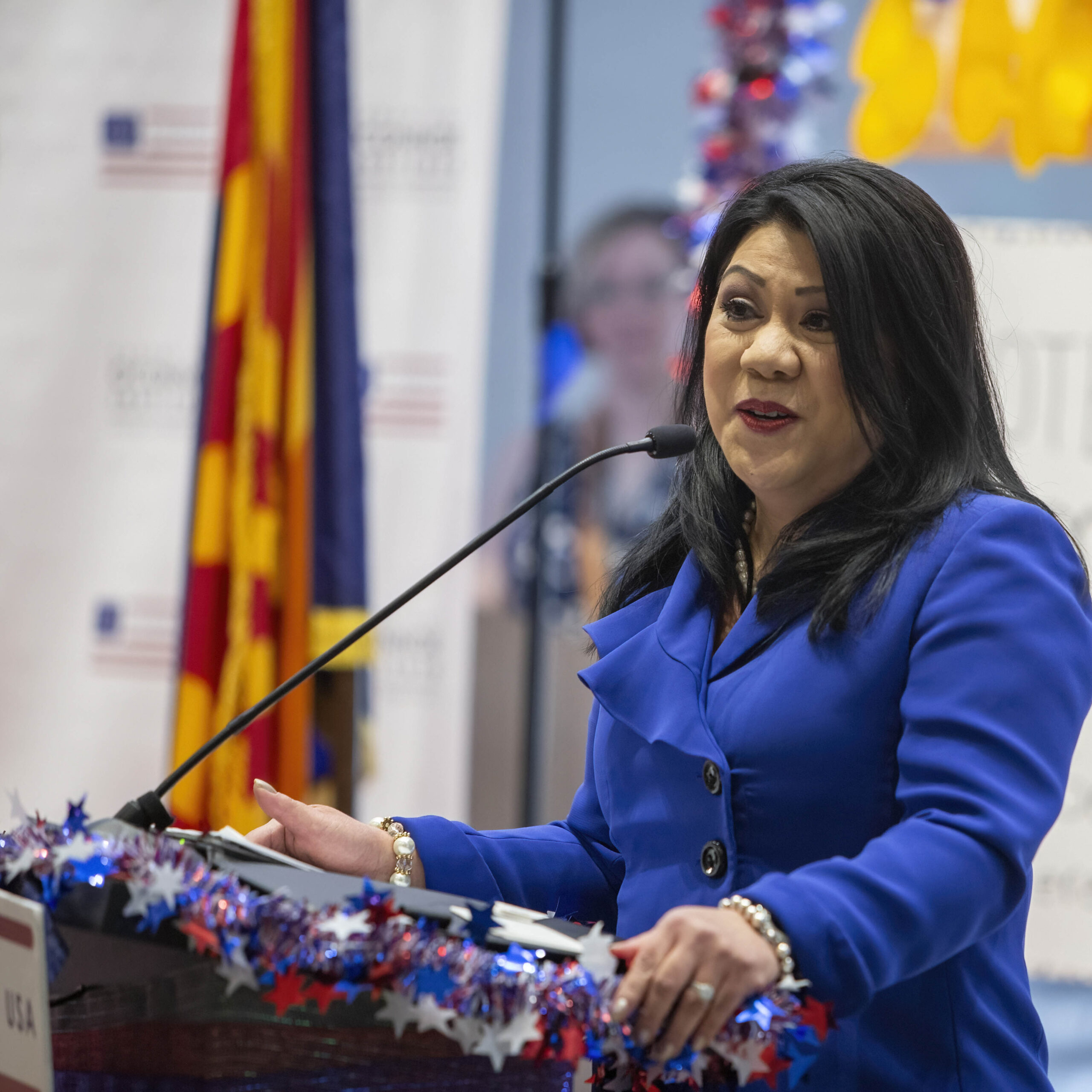 June 13, 2025 Camp SDO A woman in a blue suit speaks at a decorated podium with a microphone. Behind her are flags and a patriotic backdrop with red, white, and blue decorations, emphasizing the importance of every citizen’s voice.