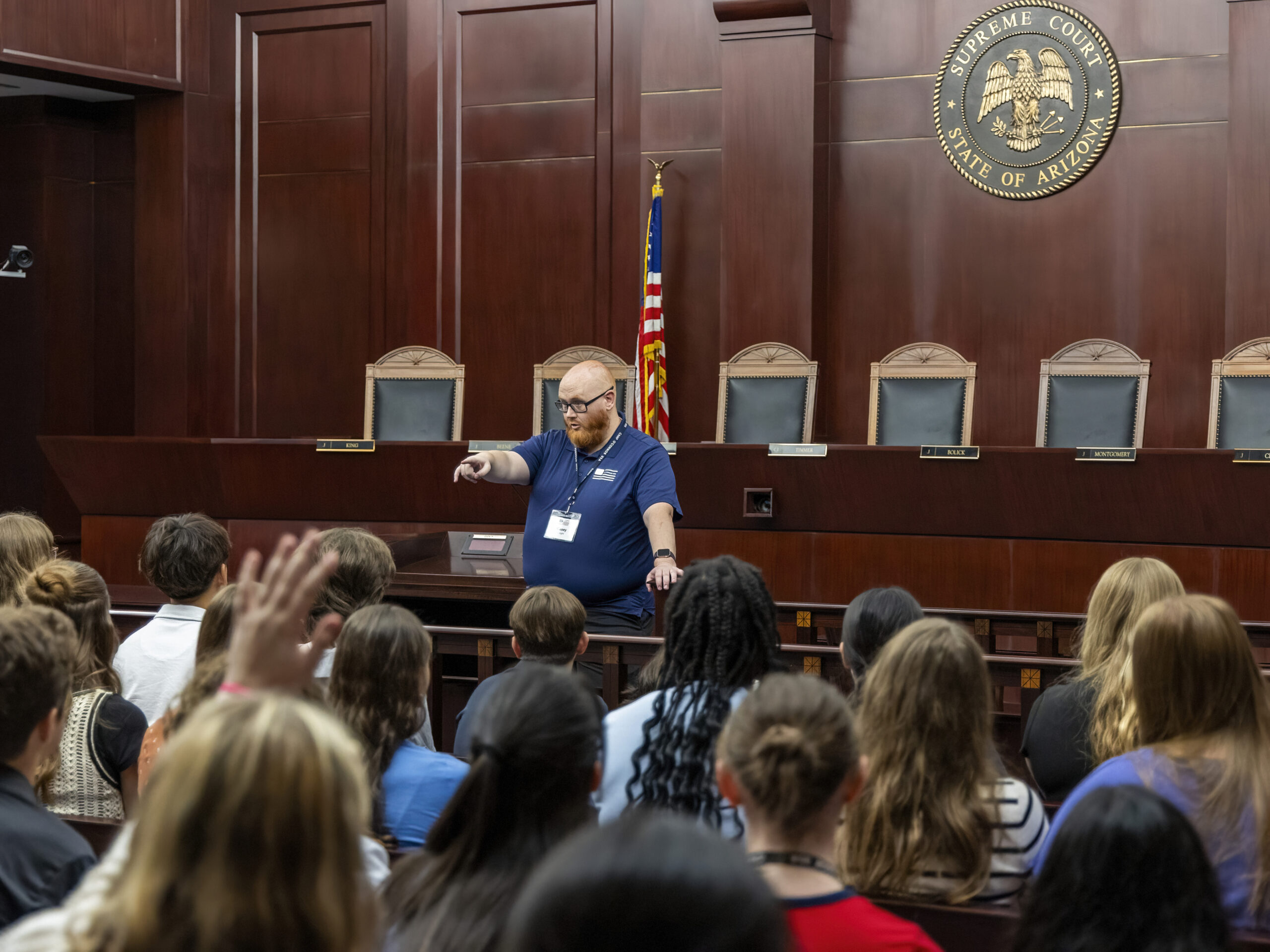 June 9, 2025 Camp SDO A man stands at the front of a courtroom, speaking to students about the role of a citizen; he points forward while they listen attentively. The room features wooden walls, an American flag, and the Arizona Supreme Court seal.