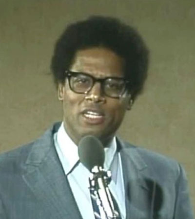 Man wearing glasses and a suit is speaking into a microphone.